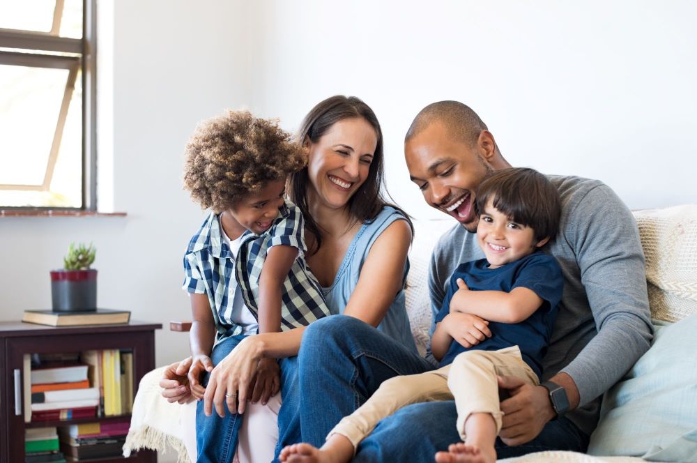 Family with two young children smiling sitting on a couch